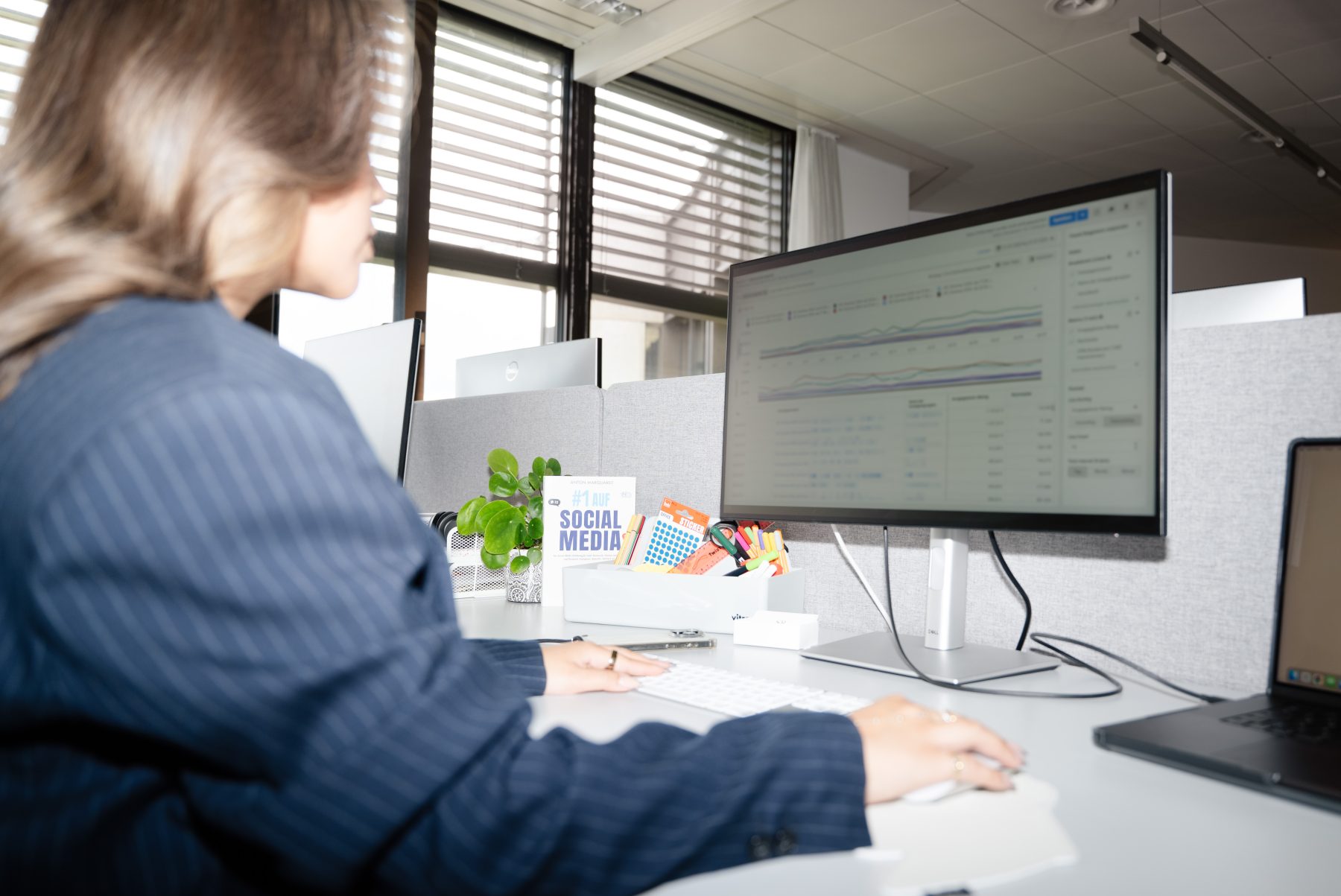 Marketing Managerin in blauem Nadelstreifenanzug sitzt an Schreibtisch und arbeitet mit Meta Ads Manager. | SR-STUDIOS