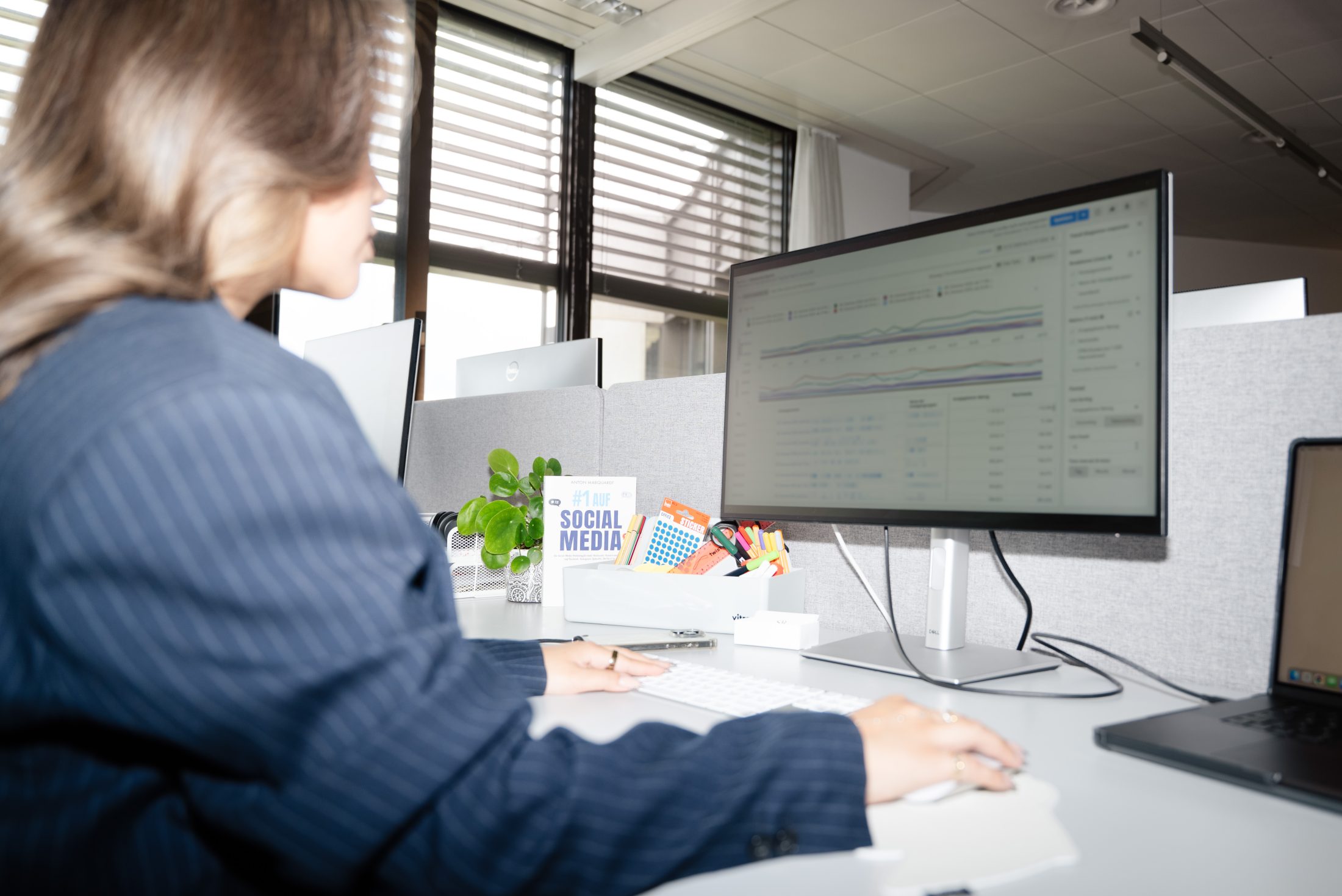 Marketing Managerin in blauem Nadelstreifenanzug sitzt an Schreibtisch und arbeitet mit Meta Ads Manager. | SR-STUDIOS