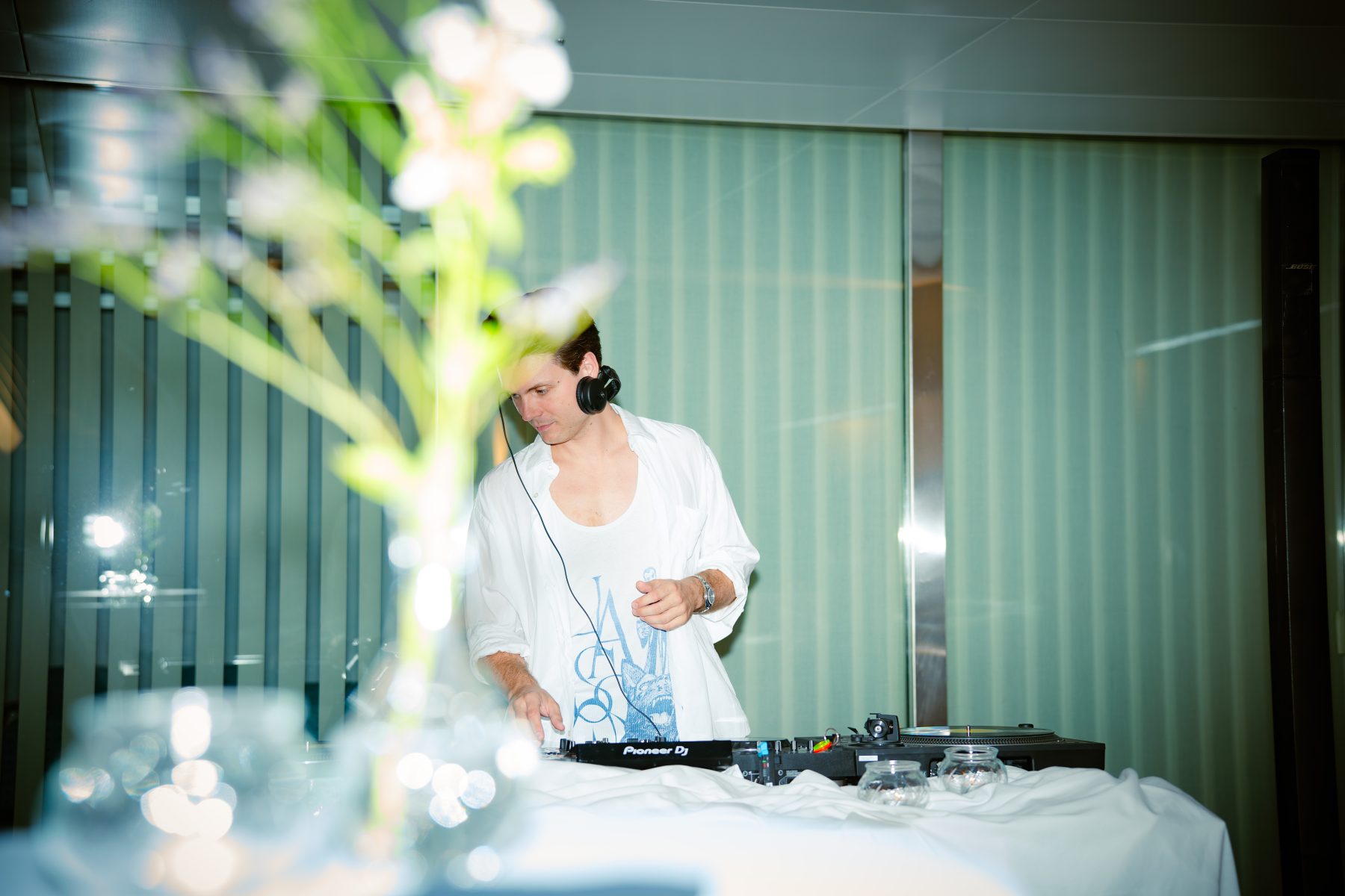 Detailaufnahme eines Mannes (DJ Floppy Disk) mit Kopfhörern im Hintergrund hinter stilvoller Dekoration. Ein DJ bedient ein Mischpult. Eventfotografie Embrace the taste by SR-STUDIOS. | SR-STUDIOS
