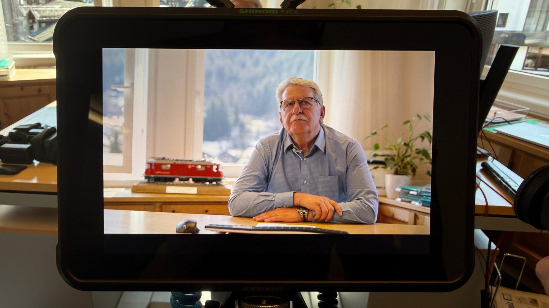 Nahaufnahme eines Monitors, der Hansueli Roth, Altgemeindepräsident von der Gemeinde Klosters, während eines Interviews für SR-STUDIOS und die Madrisa Solar AG in seinem Büro zeigt. | SR-STUDIOS