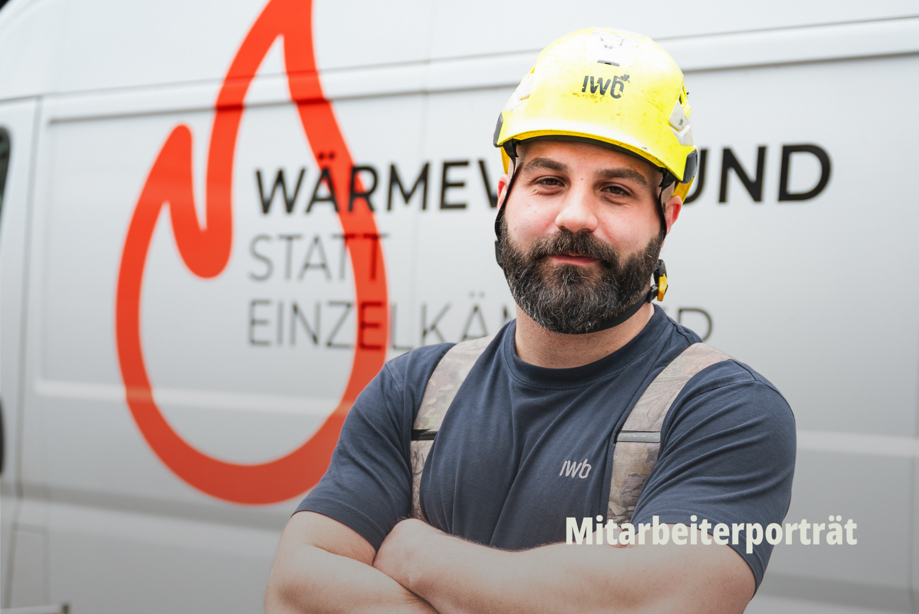 Authentisches Mitarbeiter Porträt in Arbeitskleidung vor einem Firmenwagen; IWB Experte für Fernwärme trägt Schutzhelm und hat die Arme gekreuzt während er vor einem Einsatzfahrzeug steht; Lokale Dienstleistungen; Nachhaltigkeit Basel; Tage der Sonne; IWB. | SR-STUDIOS