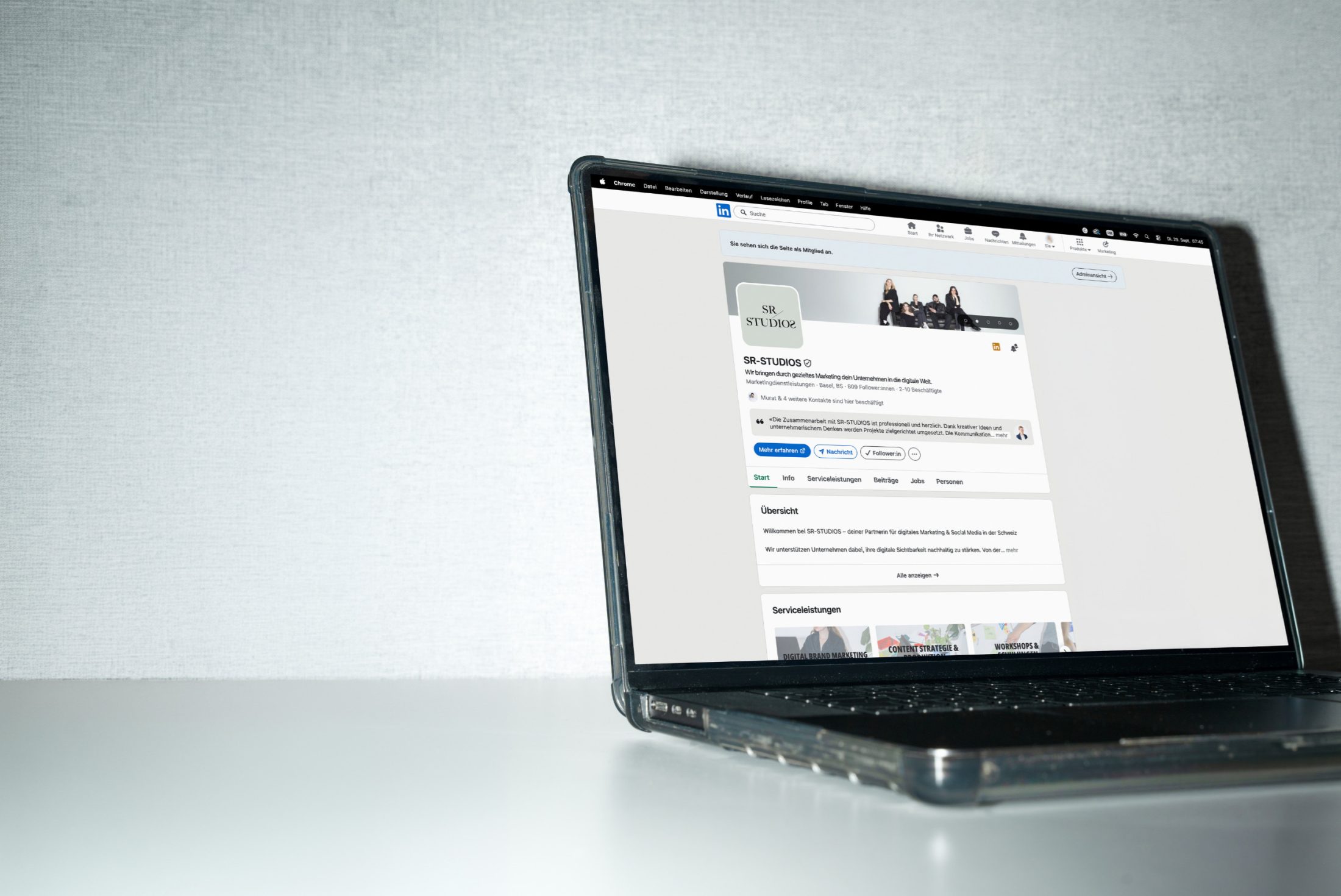 Ein Chitchat über das Marketingtool LinkedIn von SR-STUDIOS. Ein geöffneter Laptop steht auf einem weissen Tisch vor einer strukturierten, hellgrauen Wand. Auf dem Bildschirm ist die LinkedIn-Unternehmensseite von SR-STUDIOS mit dem Logo, einem Bannerfoto und verschiedenen Infobereichen zu sehen. | SR-STUDIOS