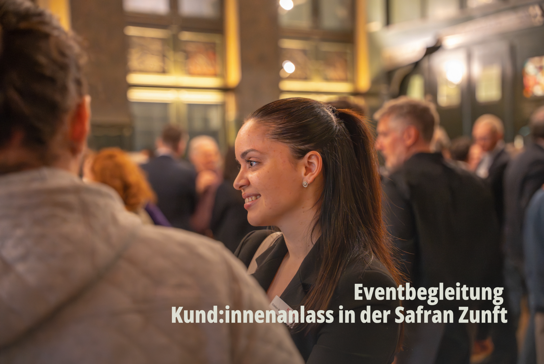 Impressionen eines Networking Gesprächs zwischen Gästen in stimmungsvoller Atmosphäre; junge Frau unterhält sich bei Raiffeisenbank Basel Kundenanlass in der Safran Zunft; Natürliche Eventbegleitung und People Fotografie von SR-STUDIOS. | SR-STUDIOS