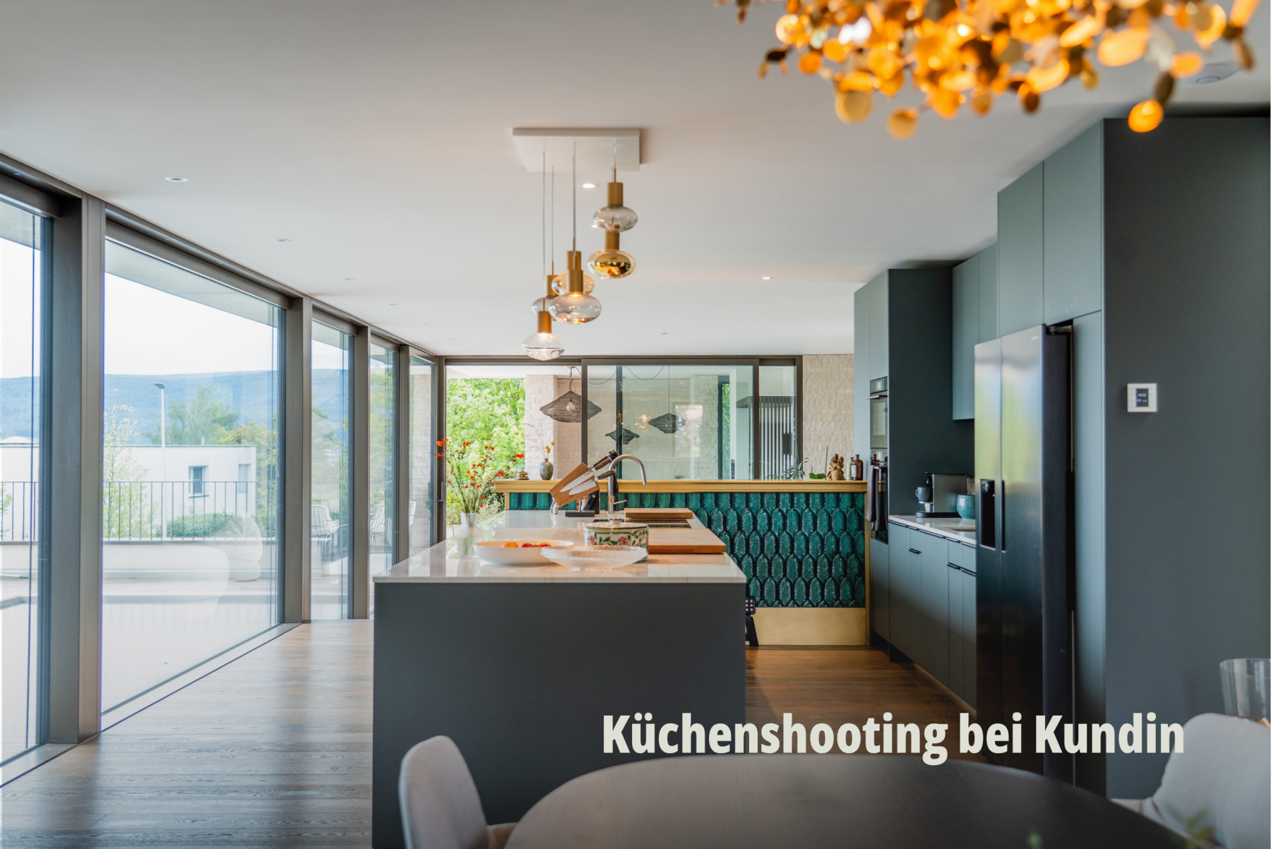 Panorama Ansicht eines modernen Wohn- und Essbereichs mit Kochinsel durch die Bard AG, dunklen Fronten und grossen Fensterfronten mit Blick ins Grüne. | SR-STUDIOS