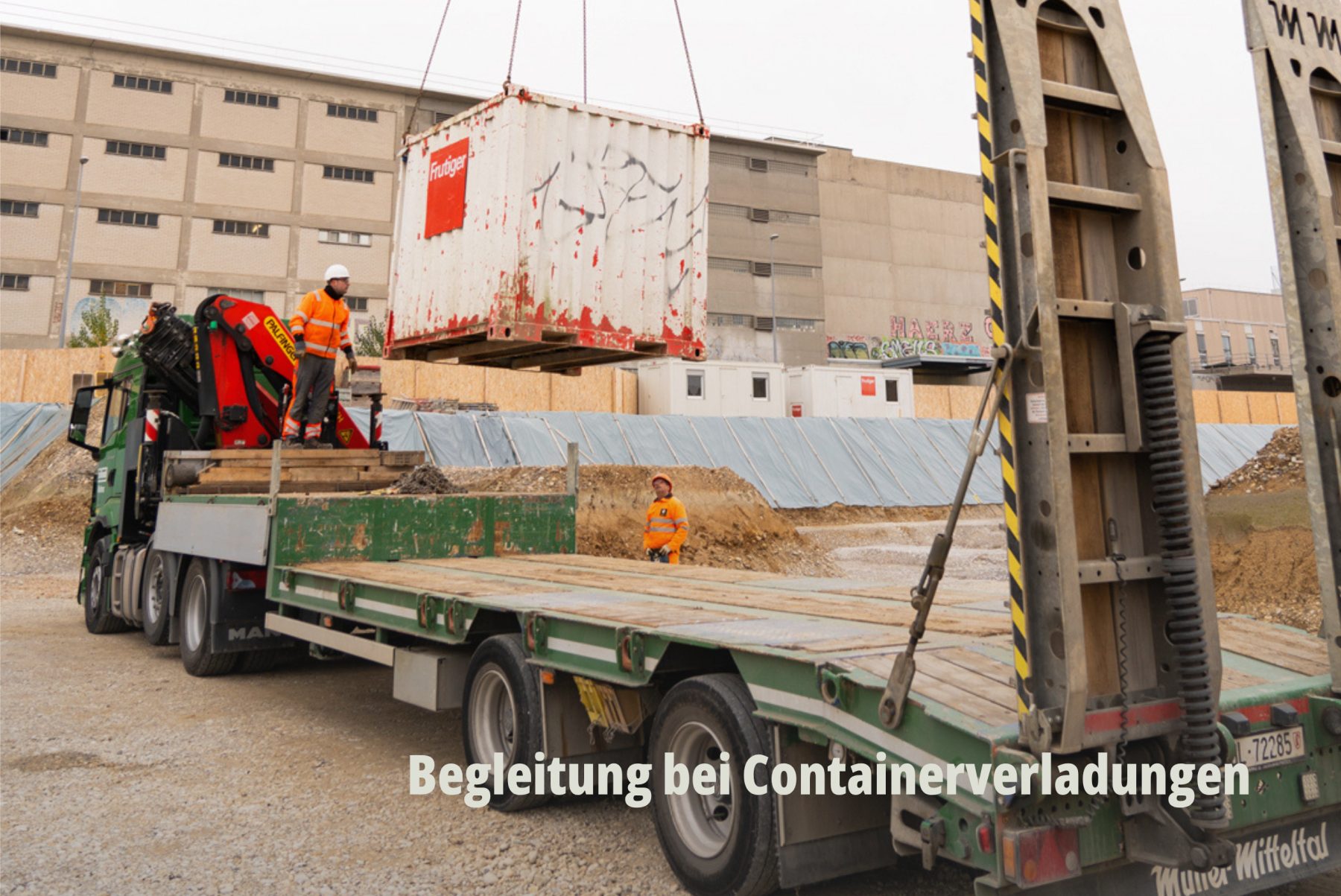 Action-Shot auf einer Baustelle: Ein Kran verlädt einen weissen Container auf einen Lastwagen der Grollimund AG. | SR-STUDIOS