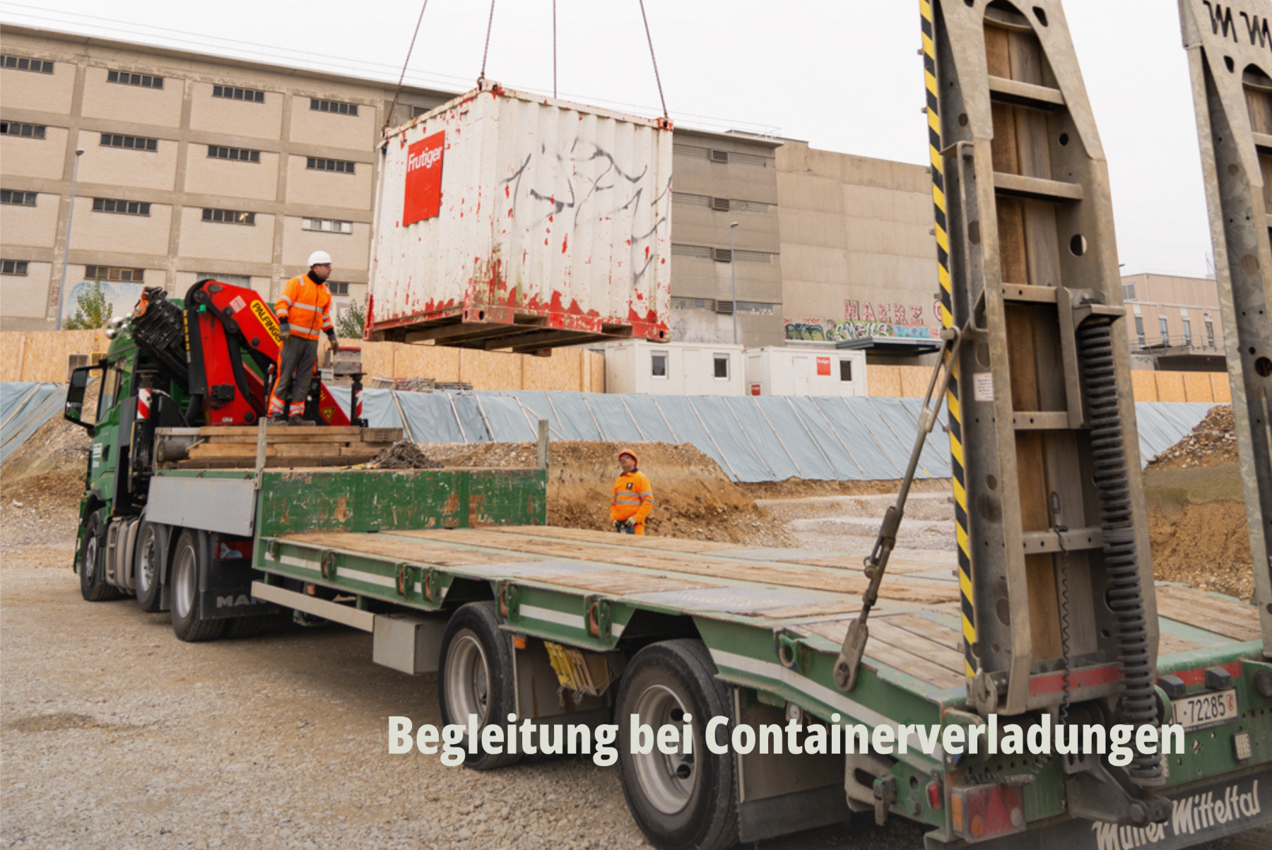 Action-Shot auf einer Baustelle: Ein Kran verlädt einen weissen Container auf einen Lastwagen der Grollimund AG. | SR-STUDIOS