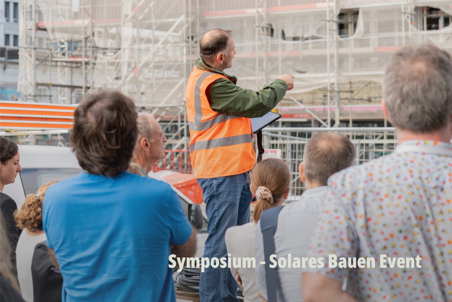 Dokumentarfotografie einer Baustellenbegehung; ein Bauleiter erklärt einer Gruppe vor einem eingerüsteten Gebäude die Planung; Planeco GmbH. | SR-STUDIOS
