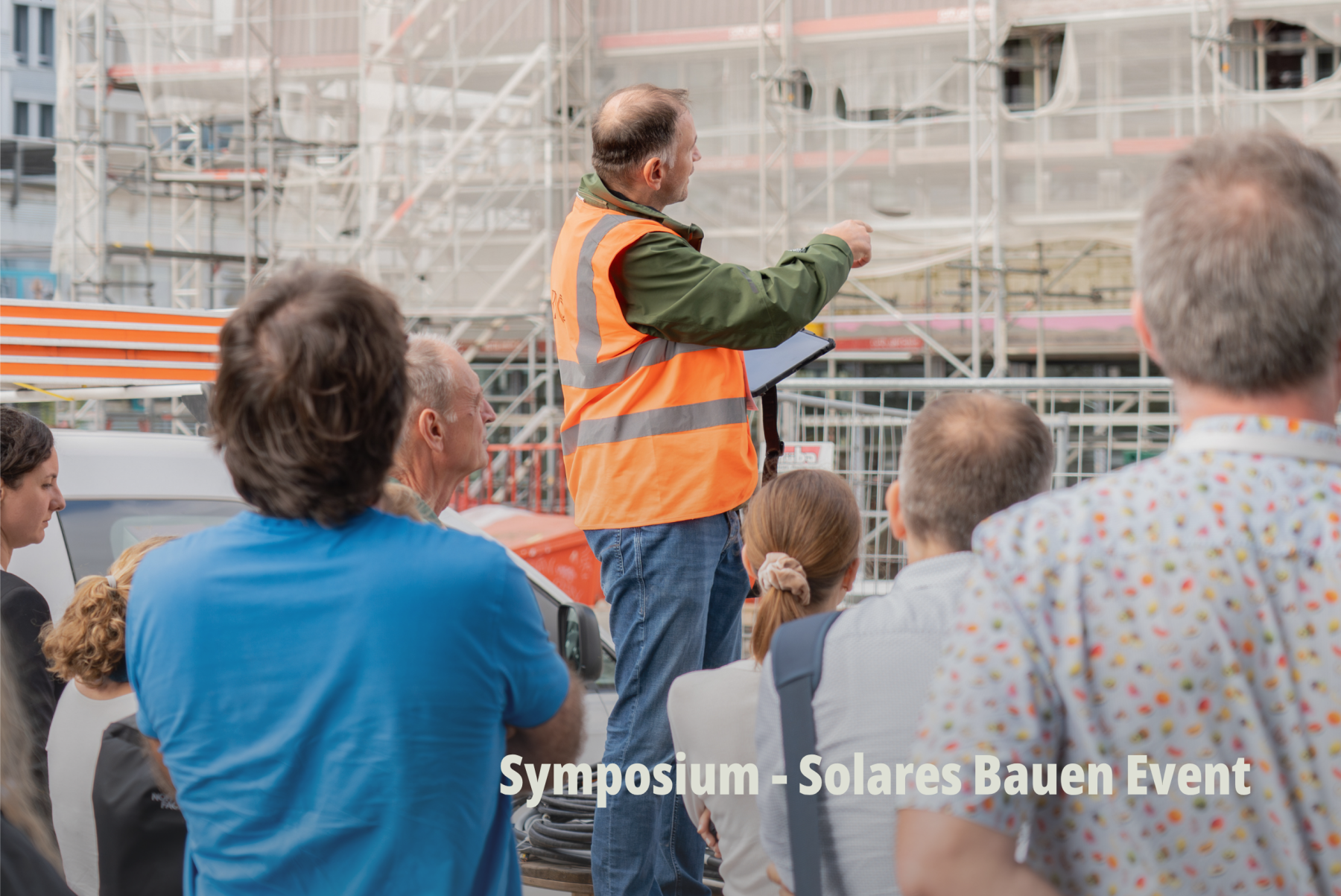 Dokumentarfotografie einer Baustellenbegehung; ein Bauleiter erklärt einer Gruppe vor einem eingerüsteten Gebäude die Planung; Planeco GmbH. | SR-STUDIOS