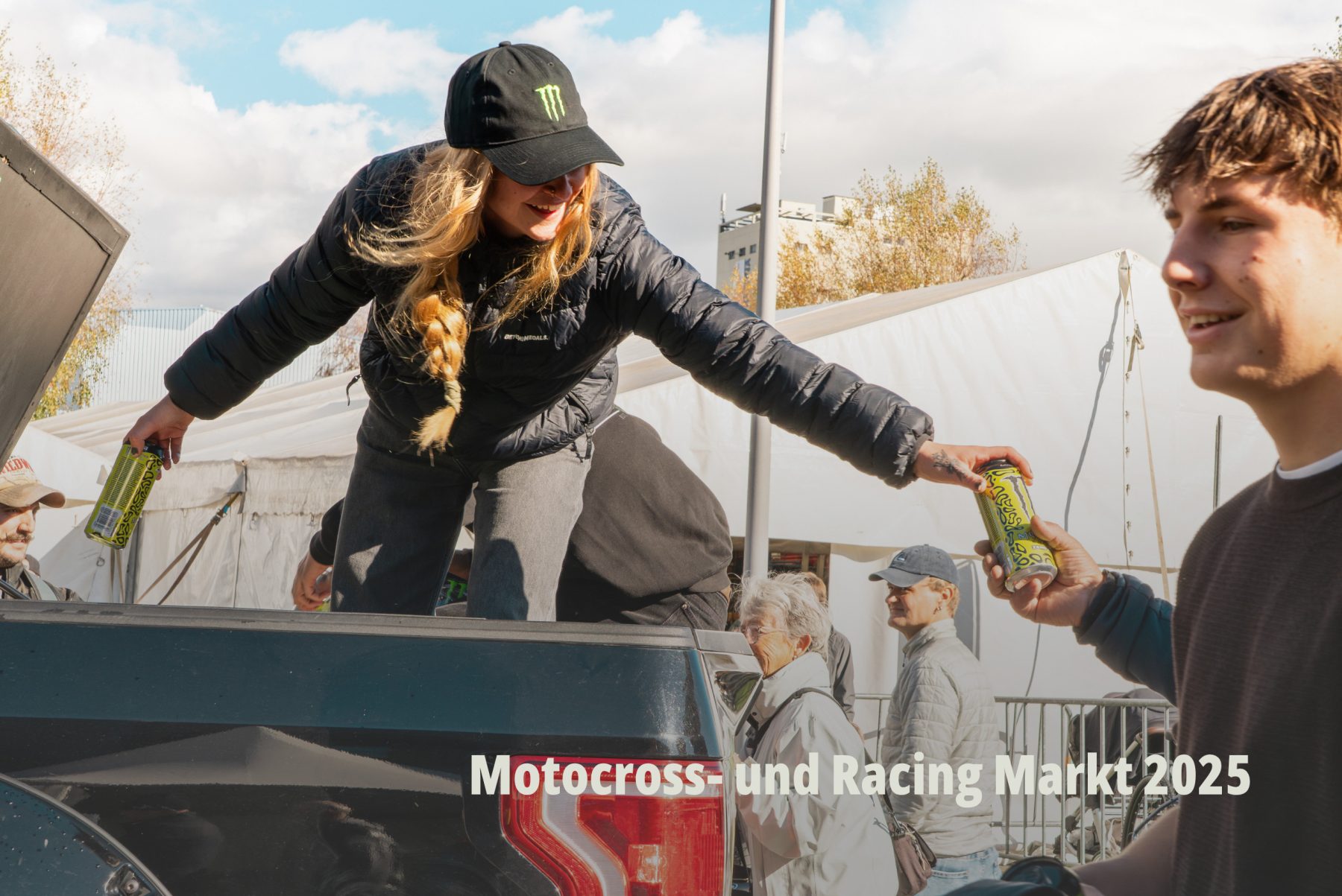 Action Shot vom Motocross- und Racing Markt 2025: Eine junge Frau mit Monster Cap verteilt Monster Energy Drinks Lando Norris Edition von einer Ladefläche eines Trucks; Eventdokumentation von SR-STUDIOS für hostettler motoren ag. | SR-STUDIOS