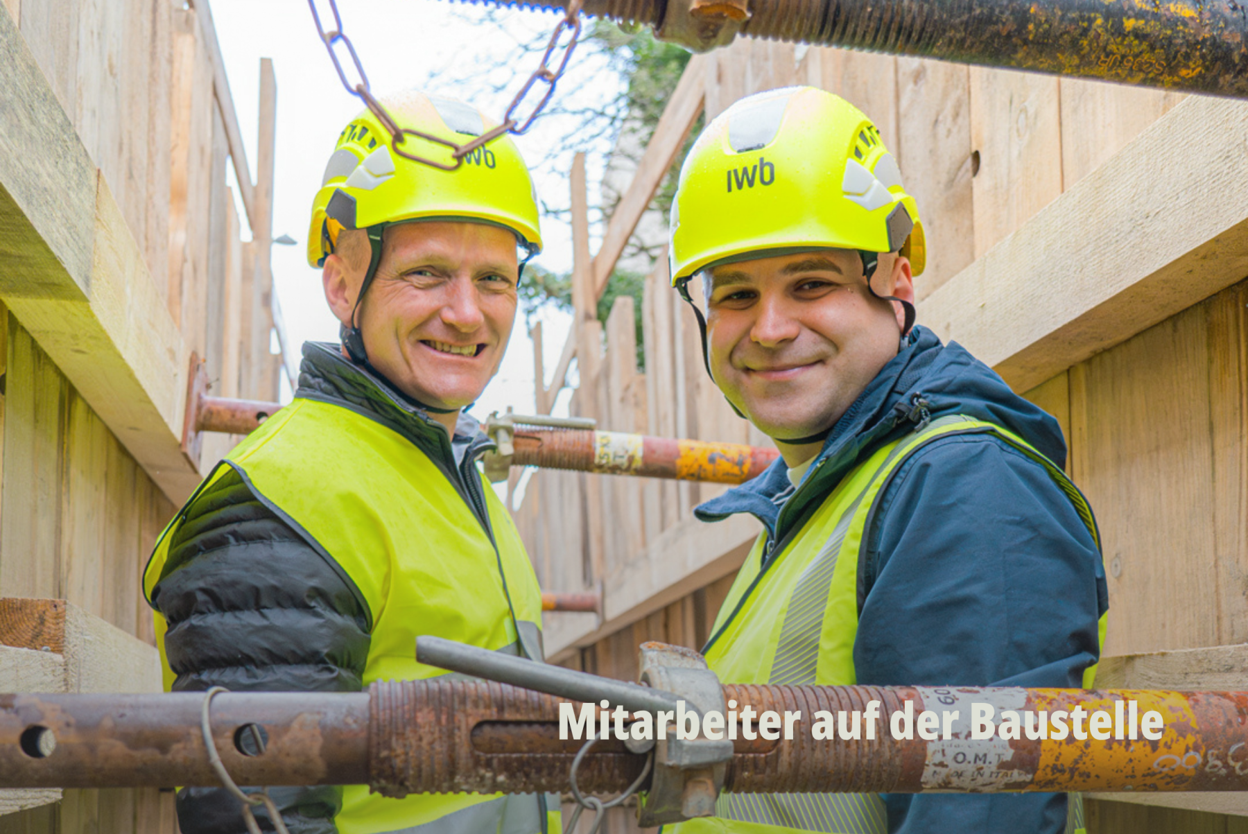 Zwei IWB Aussendienst-Mitarbeiter lächelnd in Warnwesten und Schutzhelmen bei der Arbeit auf der Baustelle; Basel Energieversorger; A Day with me; IWB. | SR-STUDIOS