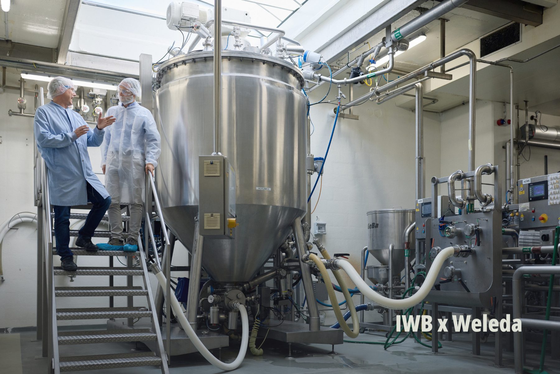 Blick in eine moderne Industrieanlage mit Fachpersonal in Schutzkleidung bei Besichtigung eines Projekts von IWB und Weleda. | SR-STUDIOS