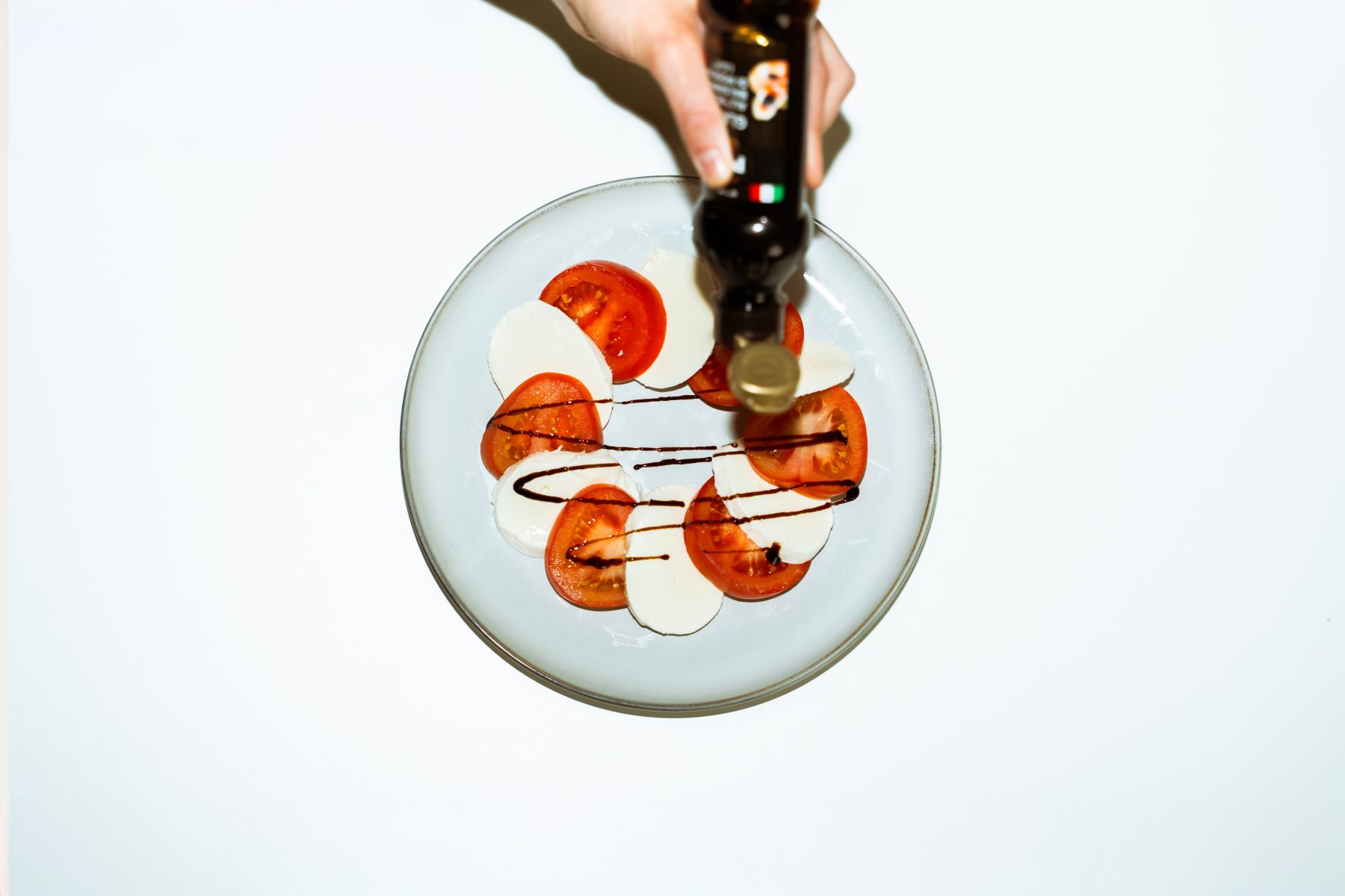 Hochwertige Food Fotografie im Digital Marketing: Balsamico Creme wird kunstvoll über einen angerichteten Tomaten Mozzarella Salat gegossen. SR-STUDIOS. | SR-STUDIOS