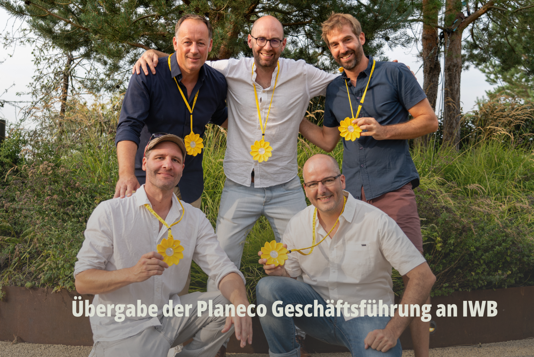Gruppenfoto eines IWB Teams im Freien, die stolz gelbe Blumenanhänger präsentieren; Übergabe der Planeco Geschäftsführung an IWB. | SR-STUDIOS