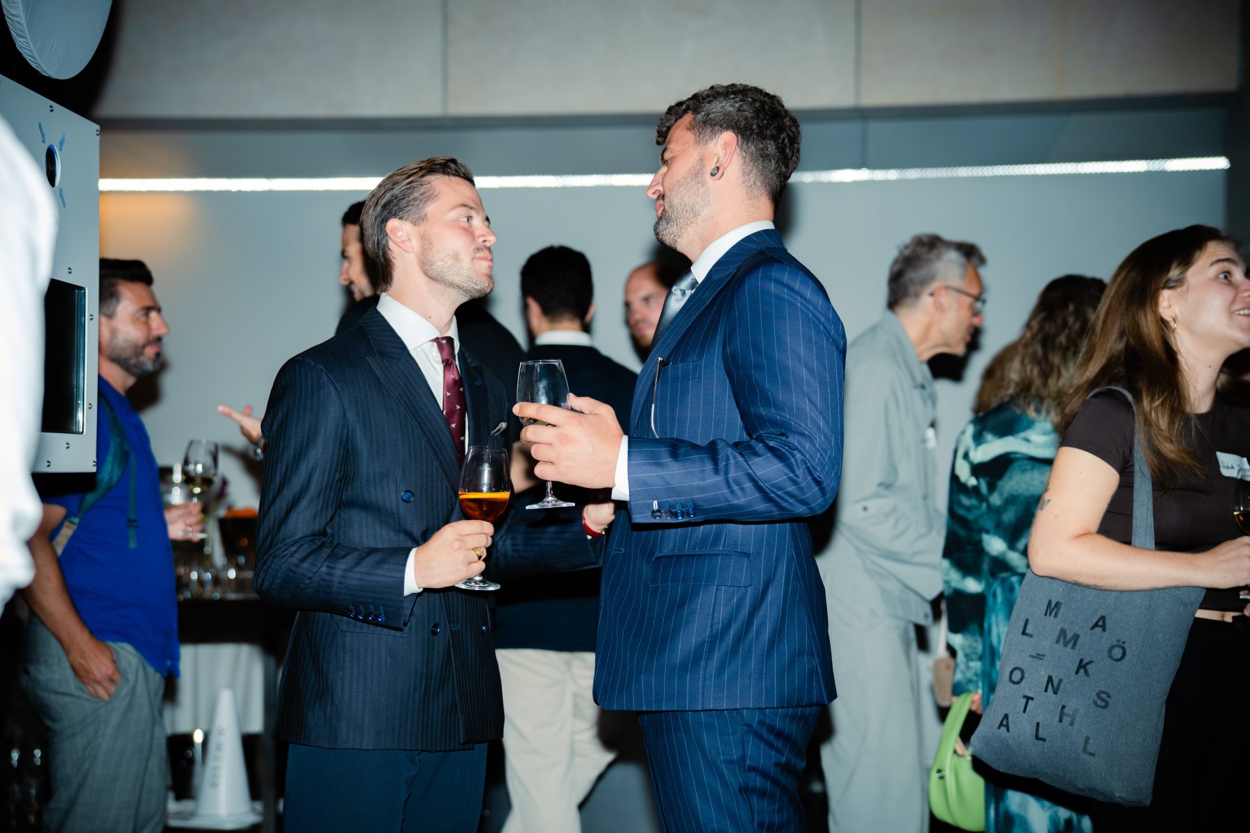 Ein Mann im blauen Anzug führt ein Gespräch mit einem Gast im Hintergrund beim Event Embrace the Taste. Embrace the taste by SR-STUDIOS. | SR-STUDIOS