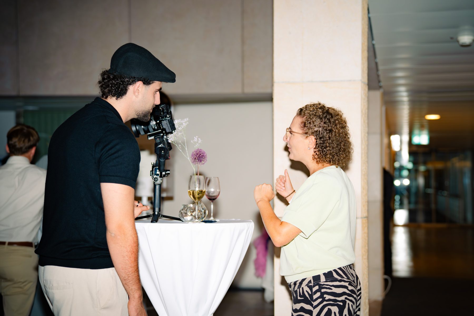 Ein Mann mit Cappy und Kamera im Gespräch mit einer Frau in weißem Top beim Event Embrace the Taste. Eventfotografie und Event Videografie Embrace the taste by SR-STUDIOS. | SR-STUDIOS