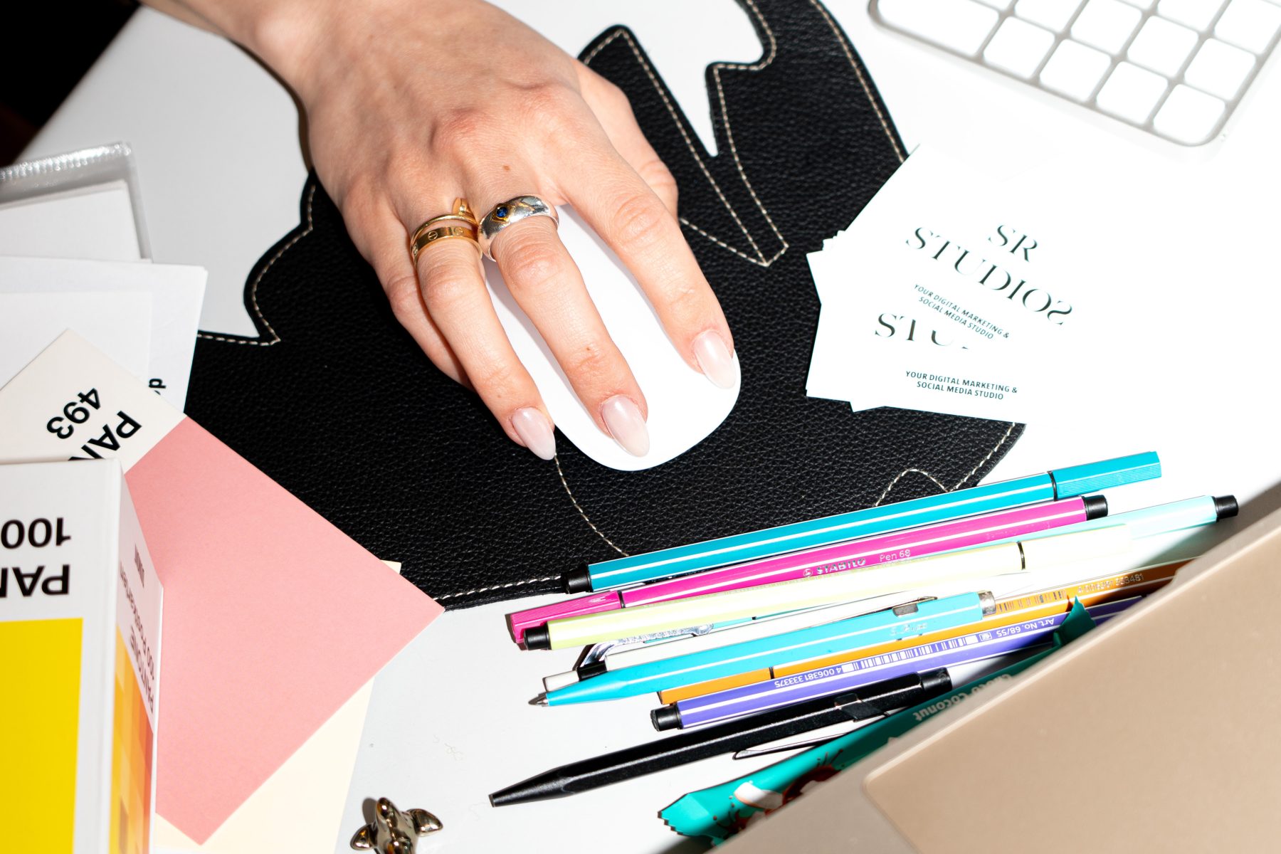 Detailshot von der Hand mit Ringen einer jungen Frau mit Laptop-Maus, Stifte auf dem Schreibtisch liegend. | SR-STUDIOS